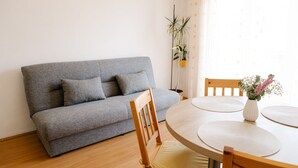 A living room with a grey sofa, wooden chairs, a round wooden table, and a vase with flowers. - Apartments Petri (Tisno)