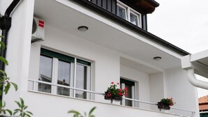 A white building with two windows, a balcony with potted plants, and an air conditioning unit. - Apartments Petri (Tisno)