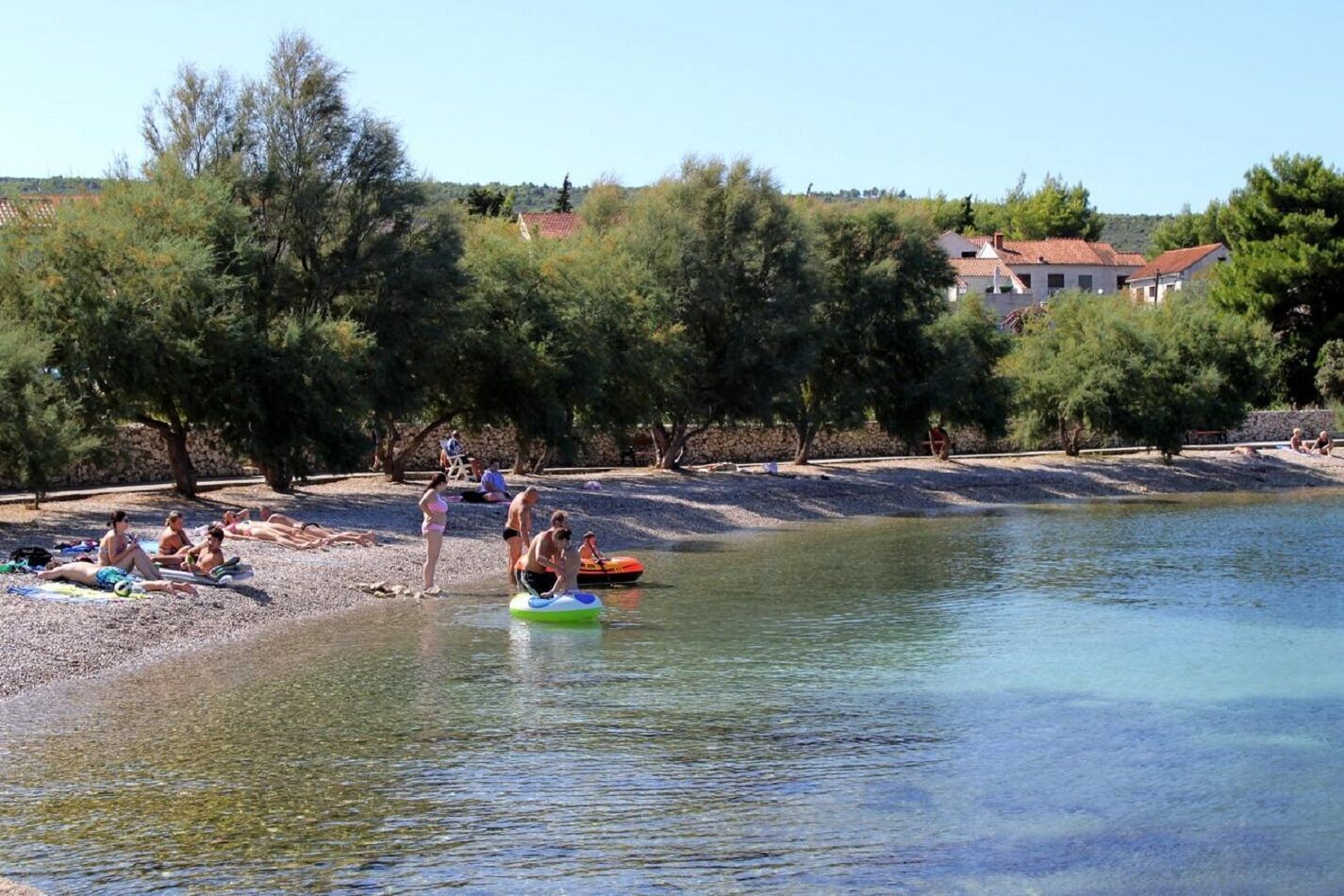 A lakeside area with people sunbathing and paddling on a boat.