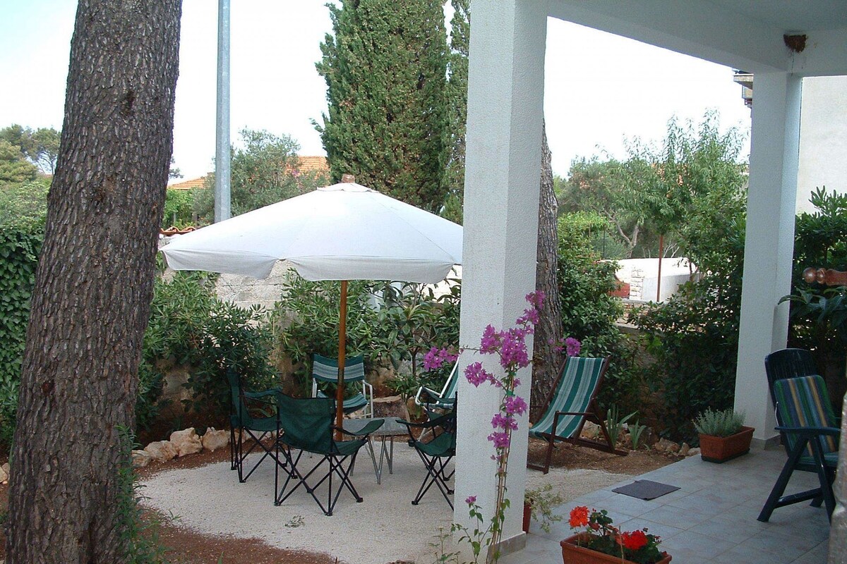 Eine Terrasse im Freien mit einem weißen Sonnenschirm, grünen Faltstühlen und Blumentöpfen.