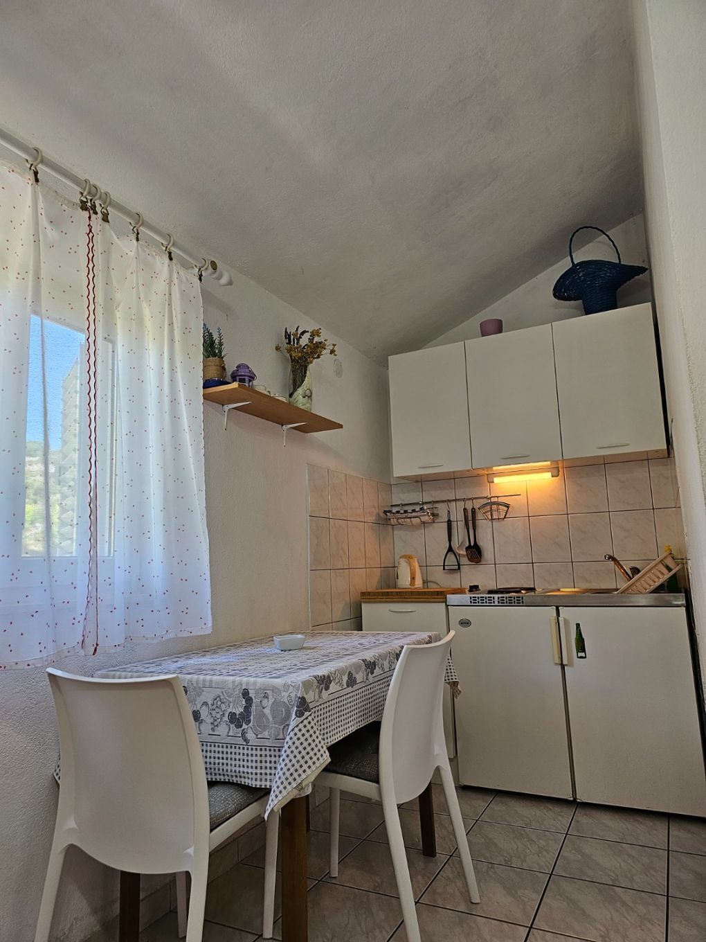 A small kitchen with white cabinets, a tiled backsplash, and a dining table with chairs.