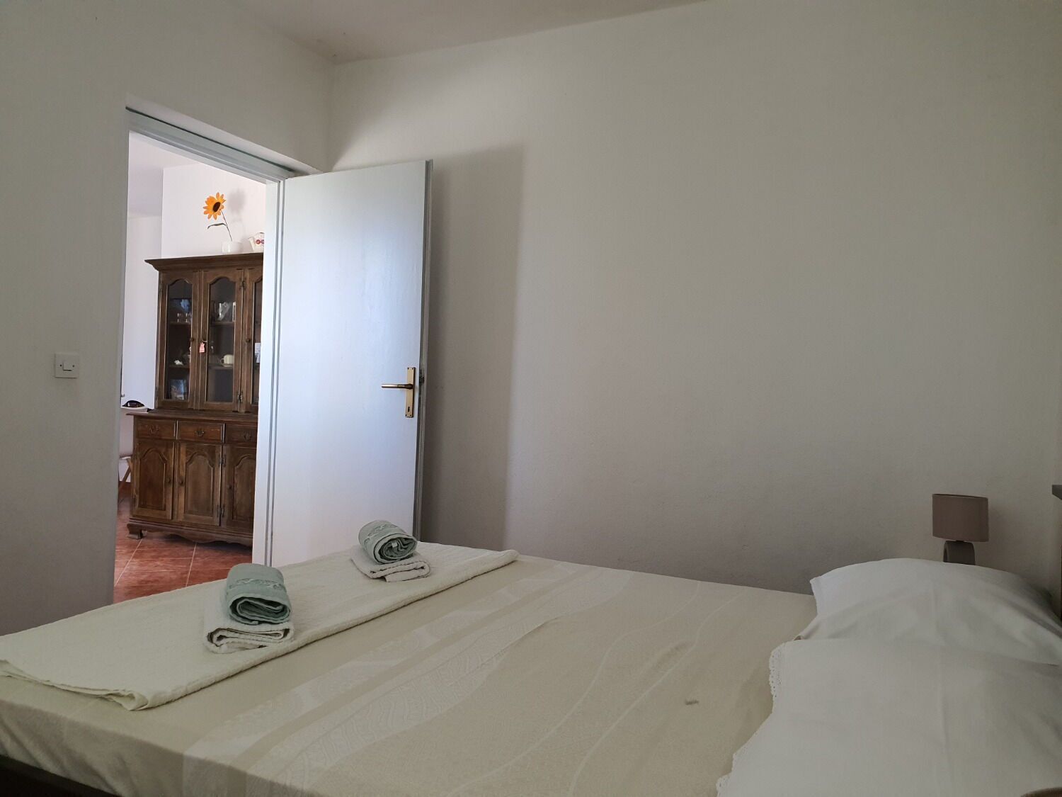 A bedroom with a bed, a nightstand, a lamp, and a wooden cabinet.