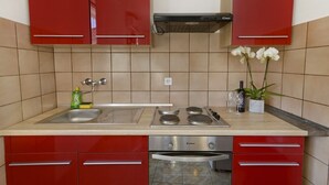 A kitchen with red cabinets, a stainless steel sink, a double oven, and a gas stove. - Apartments Ive (Tisno)
