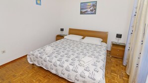A bedroom with a bed, wooden headboard, two bedside tables with lamps, a wall with a painting, and a patterned bedspread. - Apartments Ive (Tisno)