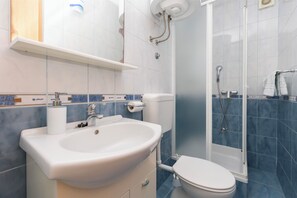 Un bagno con lavandino, wc e zona doccia, tutto in bianco.