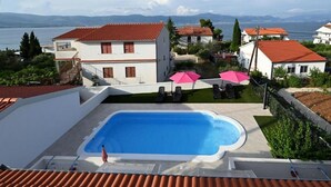 Une piscine avec vue sur la mer et les montagnes, entourée de bâtiments blancs aux toits rouges.