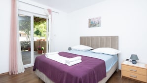 A bedroom with a bed, a nightstand, a lamp, a painting, and a sliding glass door to an outdoor area. - Apartment Bogomir (Podgora)