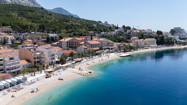 A coastal town with a beach, buildings with balconies, and a clear blue sea. - Apartment Bogomir (Podgora)