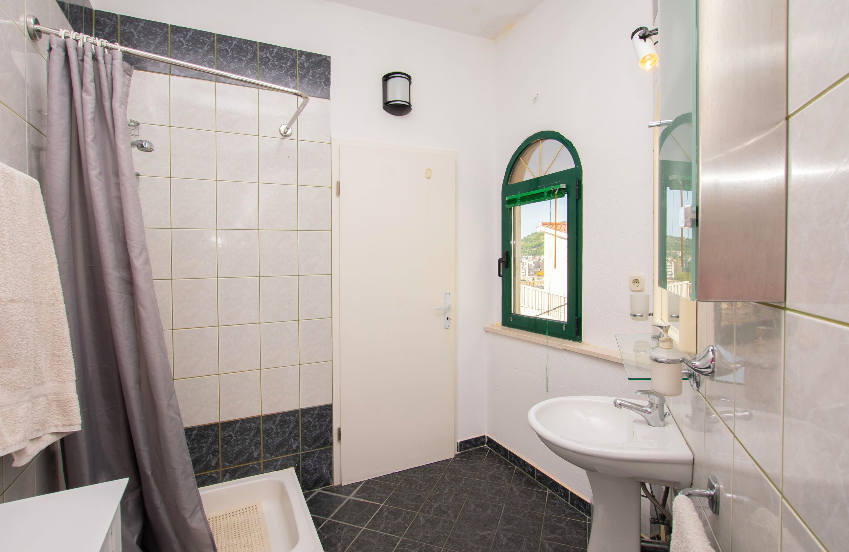 Un baño con ducha, lavabo, espejo y barra para toallas.