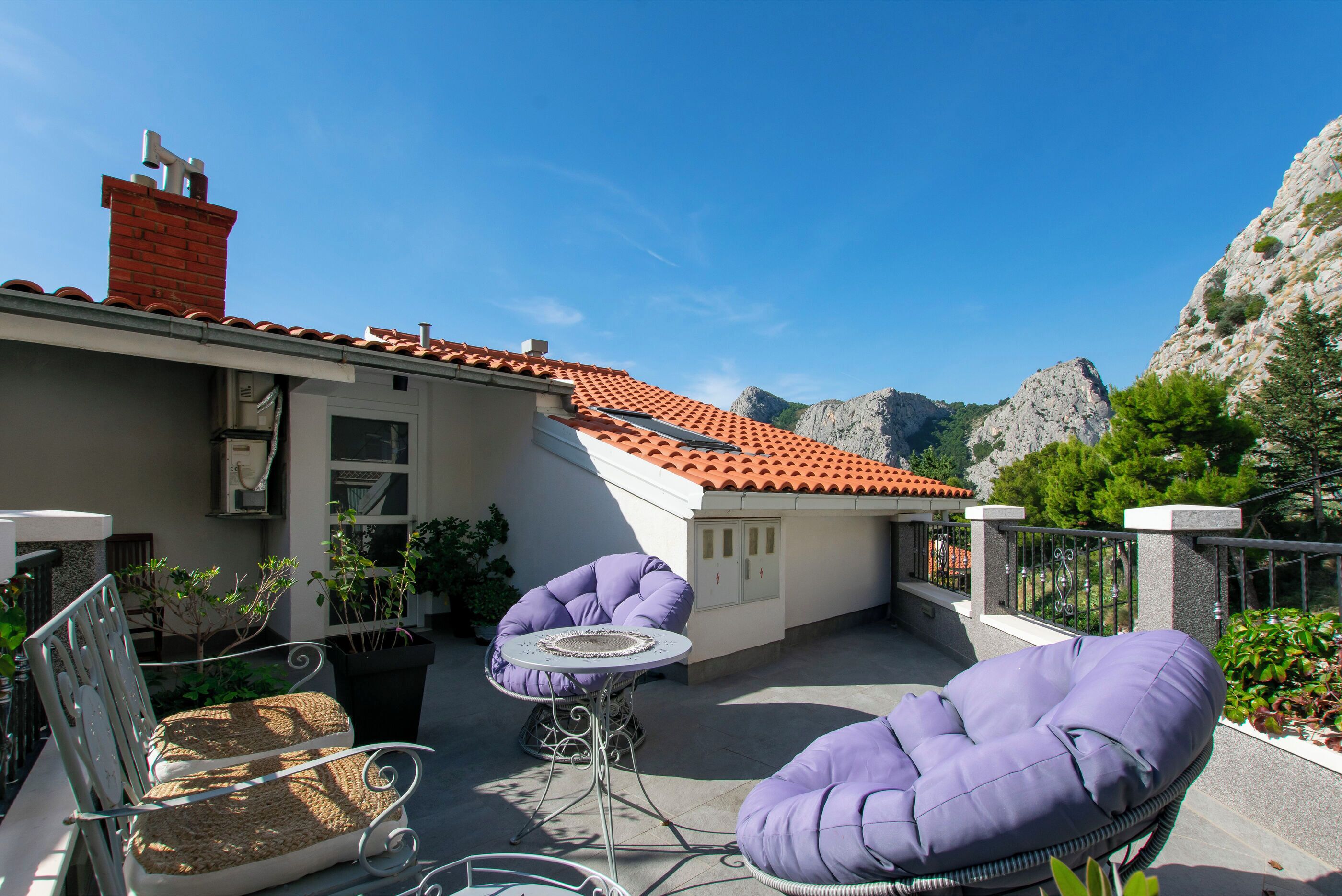 A terrace with a red-tiled roof, outdoor seating, and a view of rocky mountains.