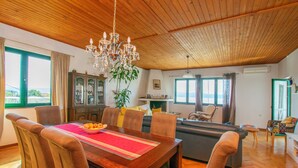 Un'ampia zona giorno con soffitto in legno, un tavolo da pranzo con sedie, un divano e un lampadario.