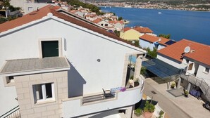 Un immeuble résidentiel doté d’un toit plat, d’un balcon avec une chaise, et offrant une vue sur une étendue d’eau et des bâtiments éloignés.