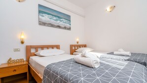 Camera d'albergo con due letti, un comodino, un quadro raffigurante il mare e applique a parete.