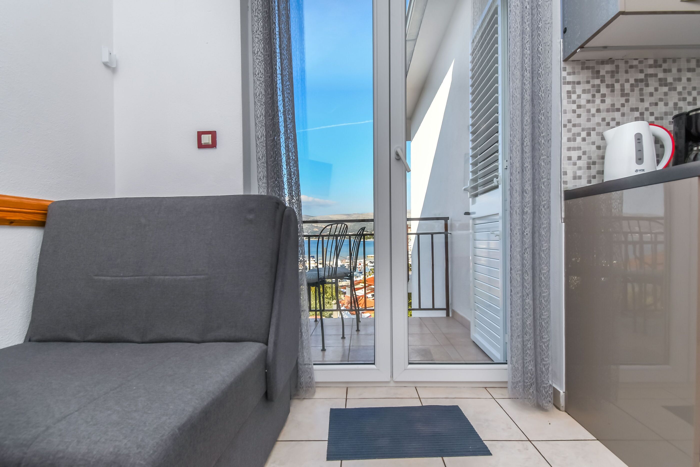 Ein Balkon mit einer Couch, Blick auf die Stadt und einer Küchenzeile mit Wasserkocher.