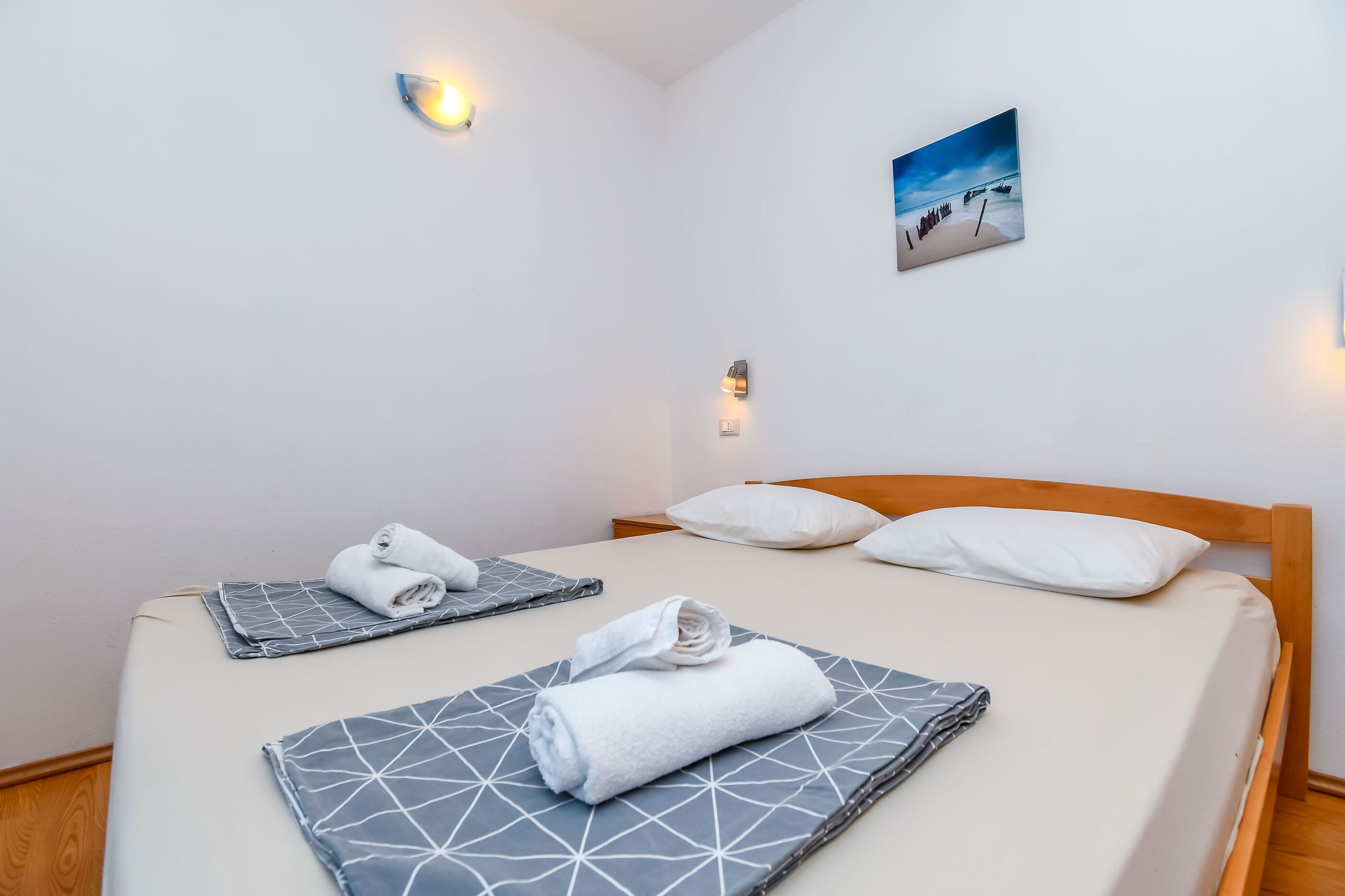 Hotelkamer met een bed, twee kussens, een aan de muur hangend schilderij en een klein wandlampje.