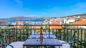 Un tavolo con una bottiglia e dei bicchieri, con vista su una cittadina costiera con edifici dai tetti rossi e un porto turistico.