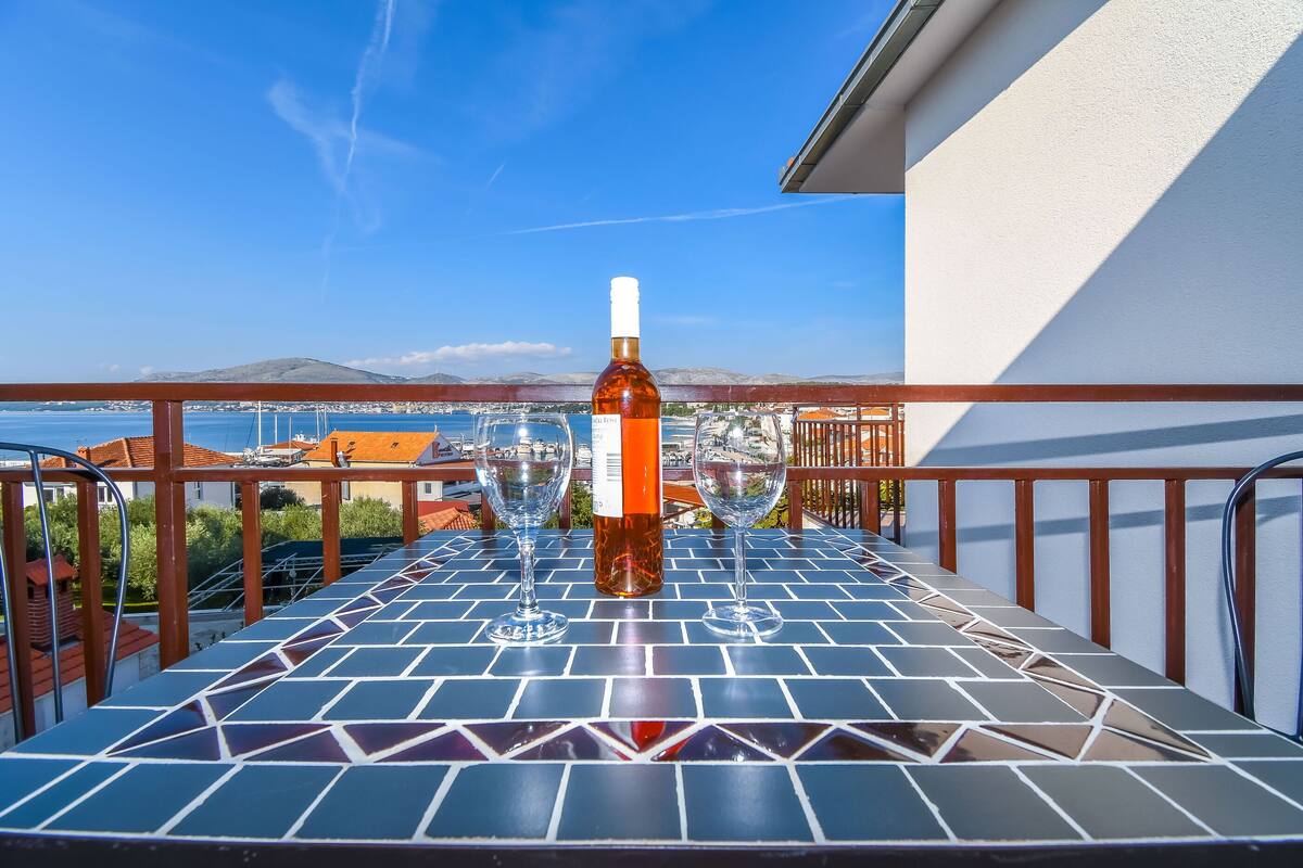 Un balcone con pavimento piastrellato, una bottiglia di vino e due bicchieri.