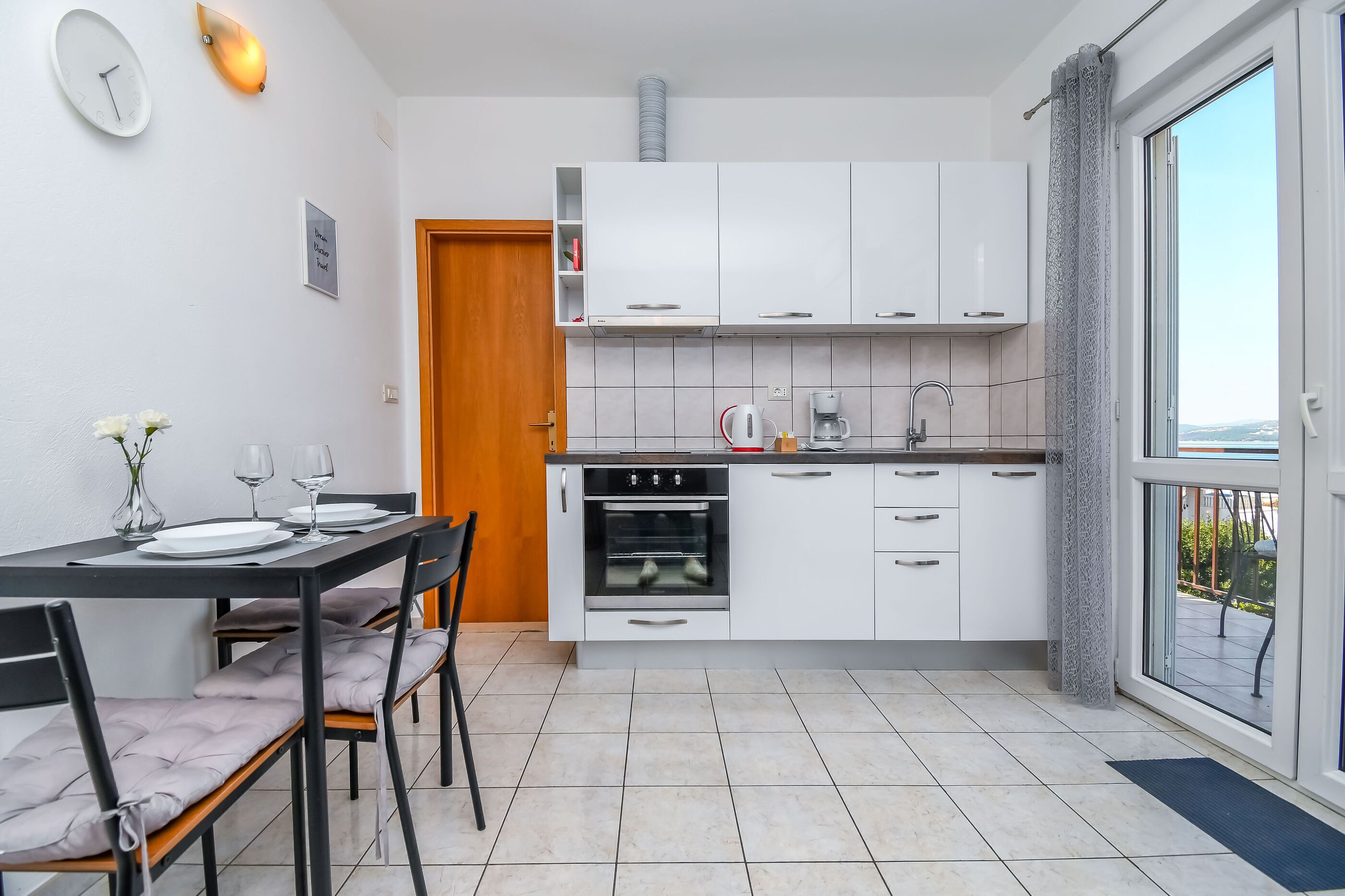 Une cuisine compacte avec des meubles blancs, un four encastré et un coin repas avec une table dressée pour deux personnes.