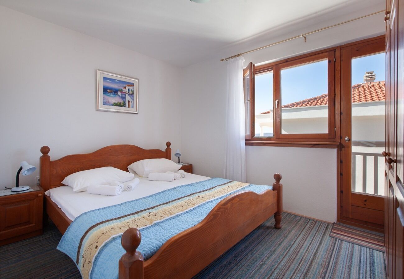 Une chambre à coucher avec un lit en bois, une table de chevet, une fenêtre donnant sur des immeubles et un tableau accroché au mur.