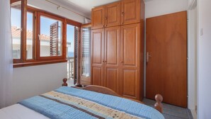 A bedroom with a bed, wooden wardrobe, and a window with a view of buildings. - Apartment Ante M (Brela)