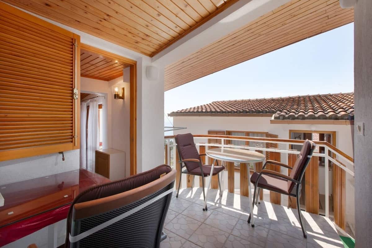A balcony with a wooden ceiling, a glass table, and two chairs.