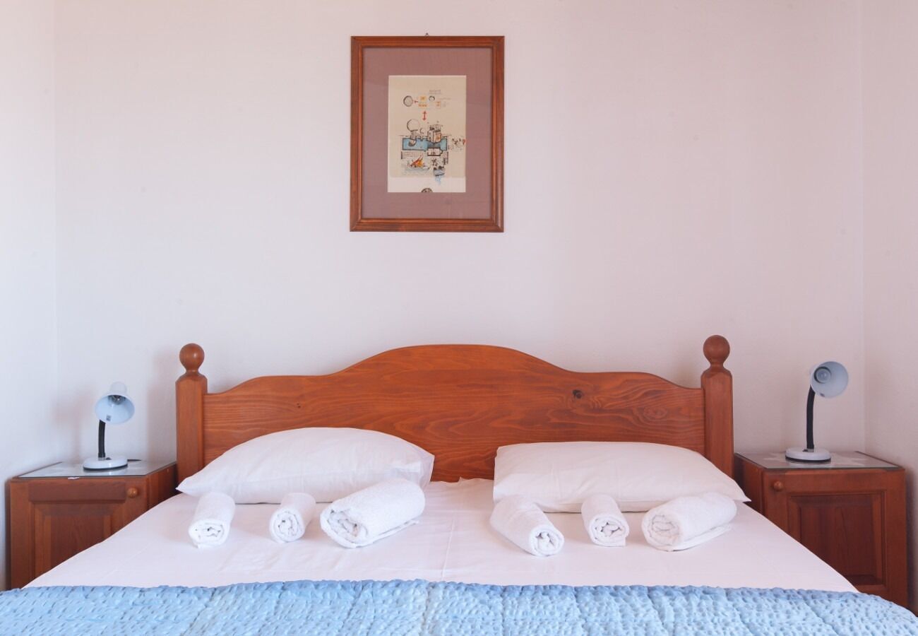 A neatly made bed with white linens and rolled towels, a wooden headboard, and a framed picture on the wall.
