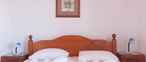 A neatly made bed with white linens and rolled towels, a wooden headboard, and a framed picture on the wall.
