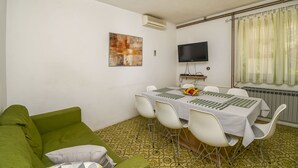 A room with a green sofa, a dining table with white chairs, a flat-screen TV, and a radiator. - Apartment Zeljko (Makarska)