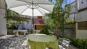 A patio with a table and chairs, a white umbrella, and a brick wall. - Apartment Zeljko (Makarska)
