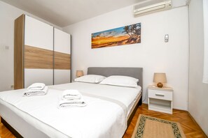 A neatly made bed with white linens and towels, a grey headboard, and a small bedside table with a lamp. - Apartment Zeljko (Makarska)