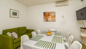 A dining area with a table set for four, a green sofa, a framed picture, and a flat-screen TV. - Apartment Zeljko (Makarska)