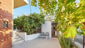 A patio area with a brick wall, a white column, two chairs, and a small garden with plants and a tree. - Apartment Ivanka (Trogir)