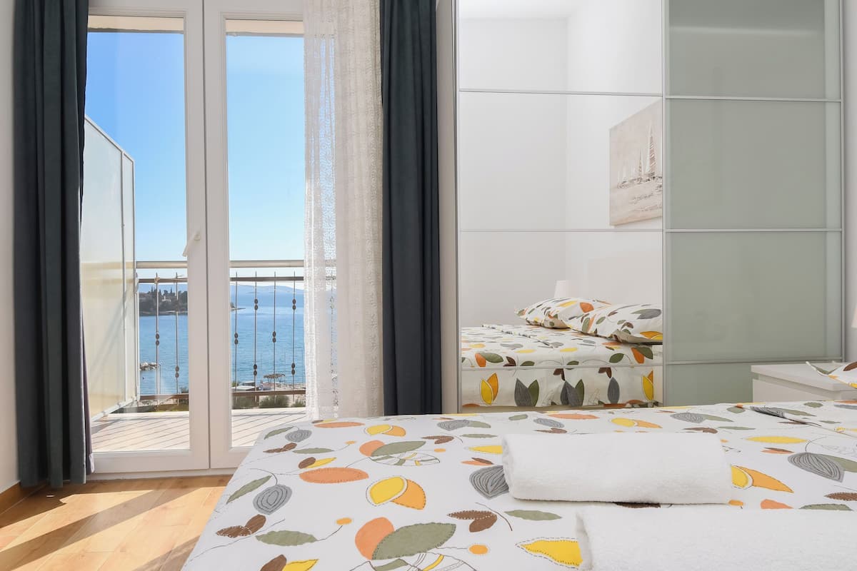 A bedroom with a bed, a nightstand, a wardrobe, and a view of the sea through a sliding door.