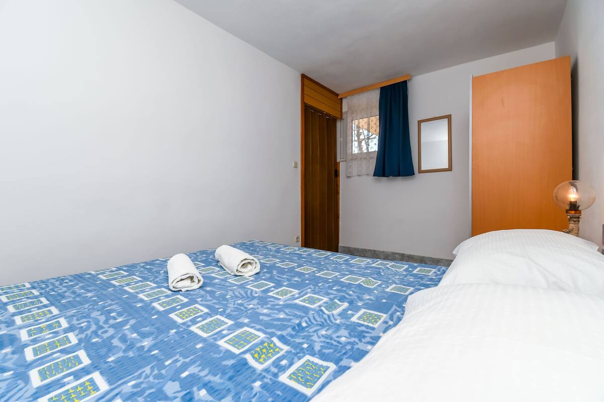 A hotel room with a bed, a window with curtains, a wooden door, and a wall-mounted lamp.