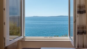 A room with a large window offering a view of the sea and distant hills. - Apartment Daniela (Okrug)