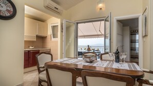 A dining area with a table set for four, a kitchen in the background, and a balcony with a view. - Apartment Daniela (Okrug)