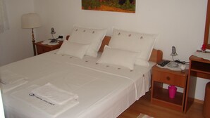Ein ordentlich bezogenes Bett mit weißen Leinen und Kissen, ein Nachttisch mit Lampe, ein weiterer Nachttisch mit Telefon und Ladegerät sowie ein Gemälde an der Wand.