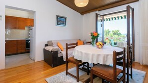 A cozy living area with a round table, wooden chairs, a sofa, and a kitchen in the background. - Apartments Nada (Brela)