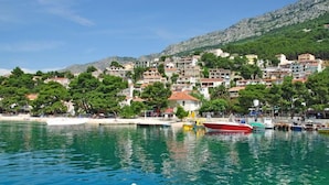 A coastal town with buildings on a hillside, a marina with boats, and a clear blue sea. - Apartments Nada (Brela)