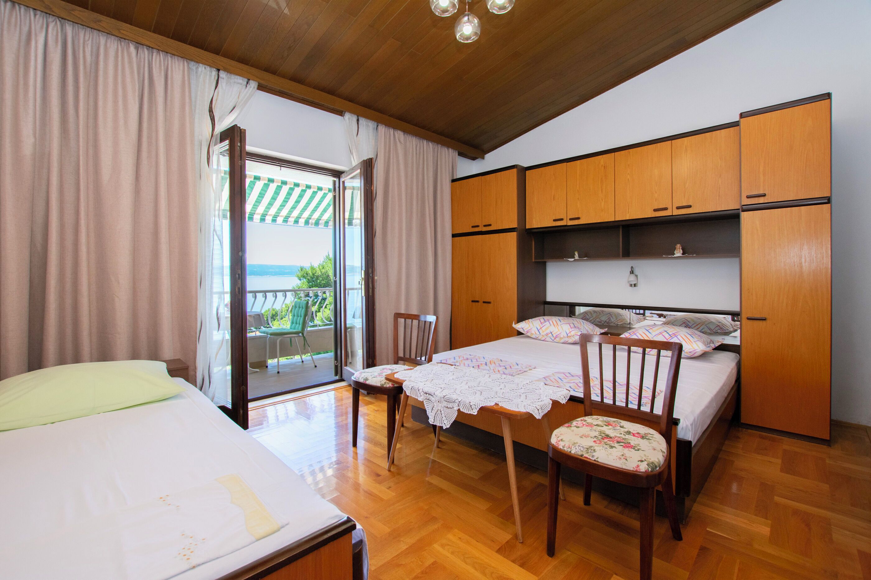A bedroom with a bed, two chairs, wooden cabinets, and a view of the outdoors.
