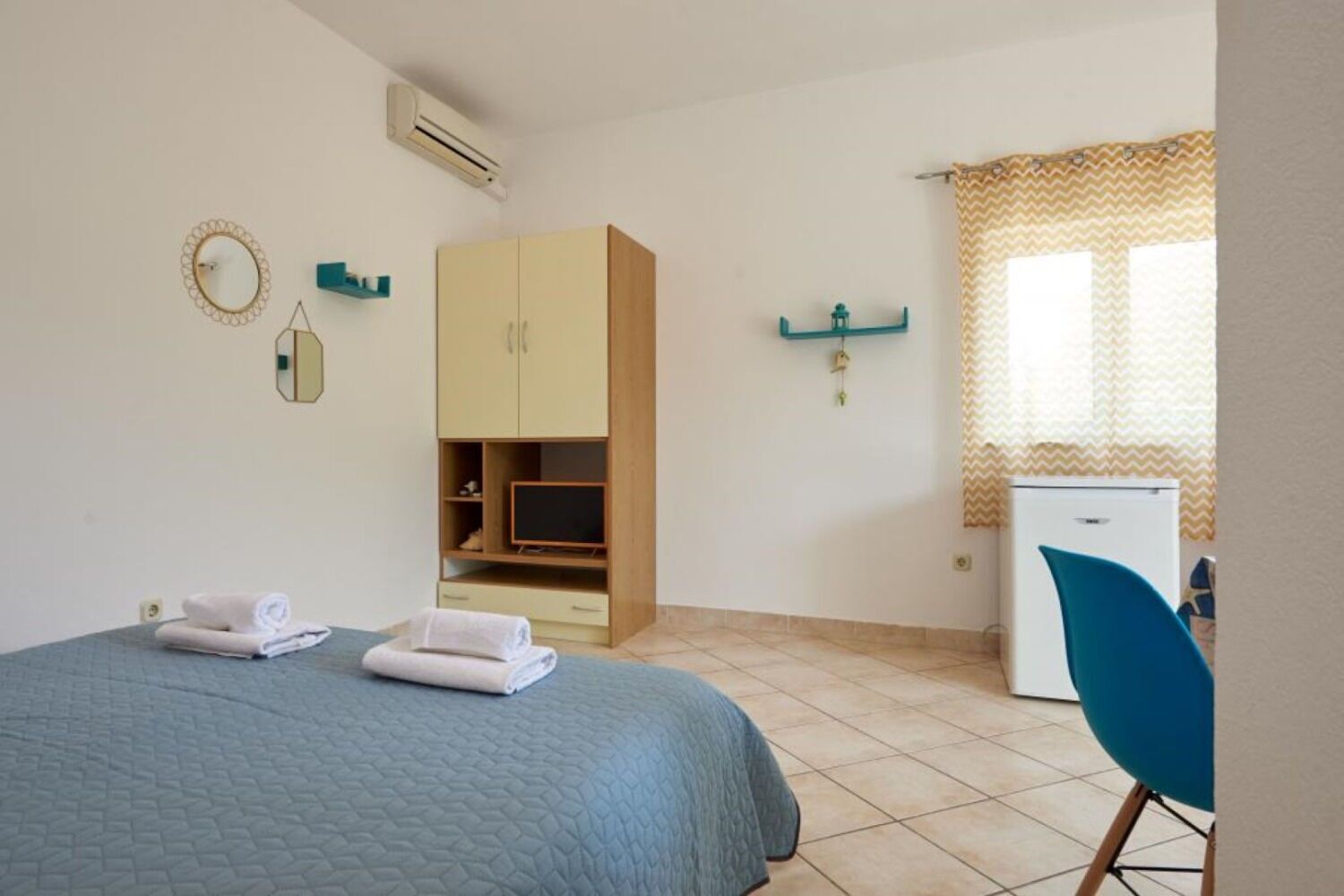 A bedroom with a bed, a wardrobe, a desk, a chair, a mirror, and a window with curtains.
