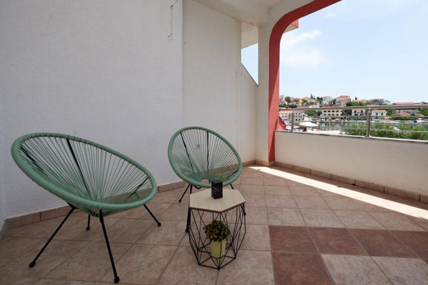Een balkon met twee groene stoelen en een kleine tafel, een bloempot en uitzicht op gebouwen over het water.