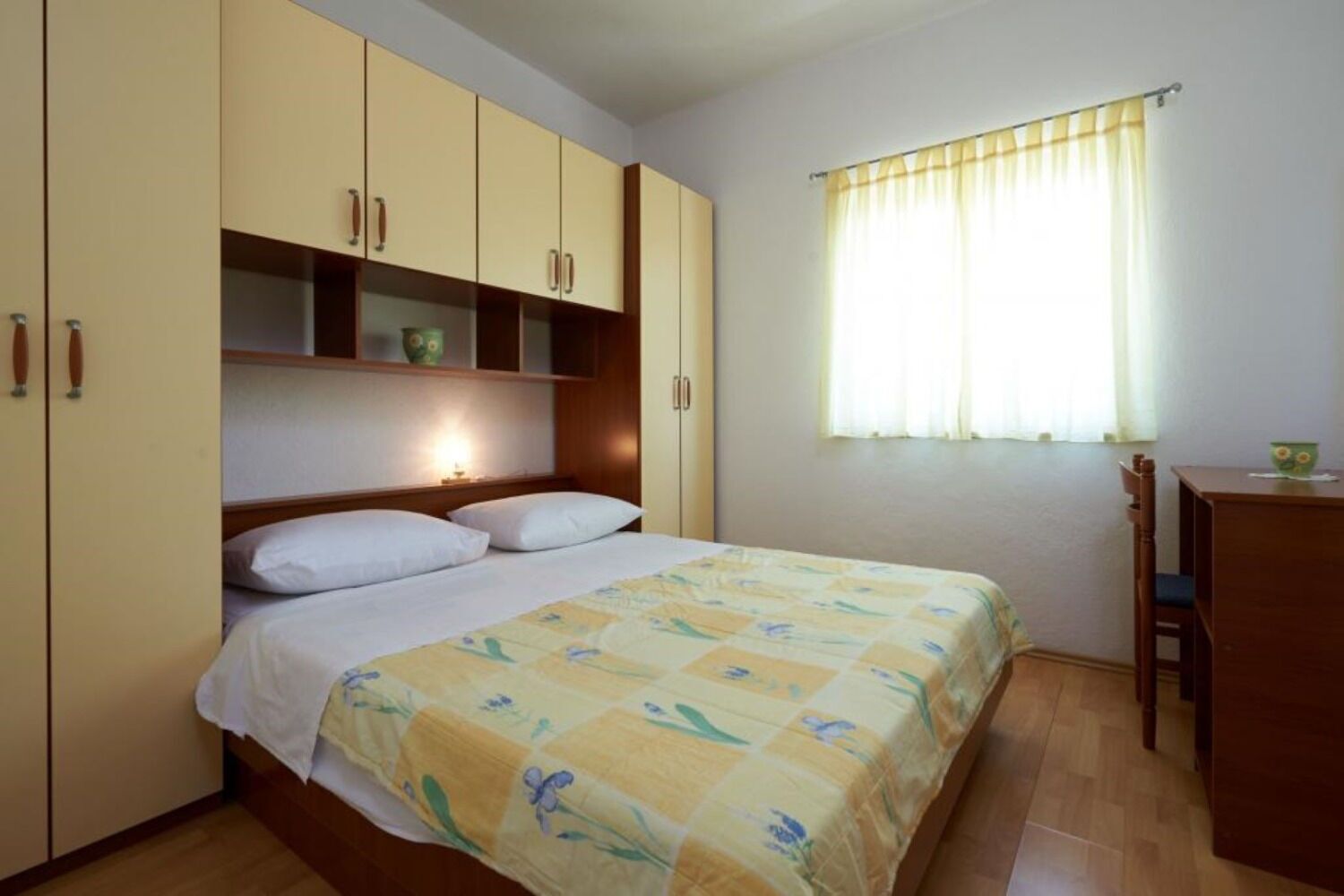 A bedroom with a bed, a desk, and a window with curtains.