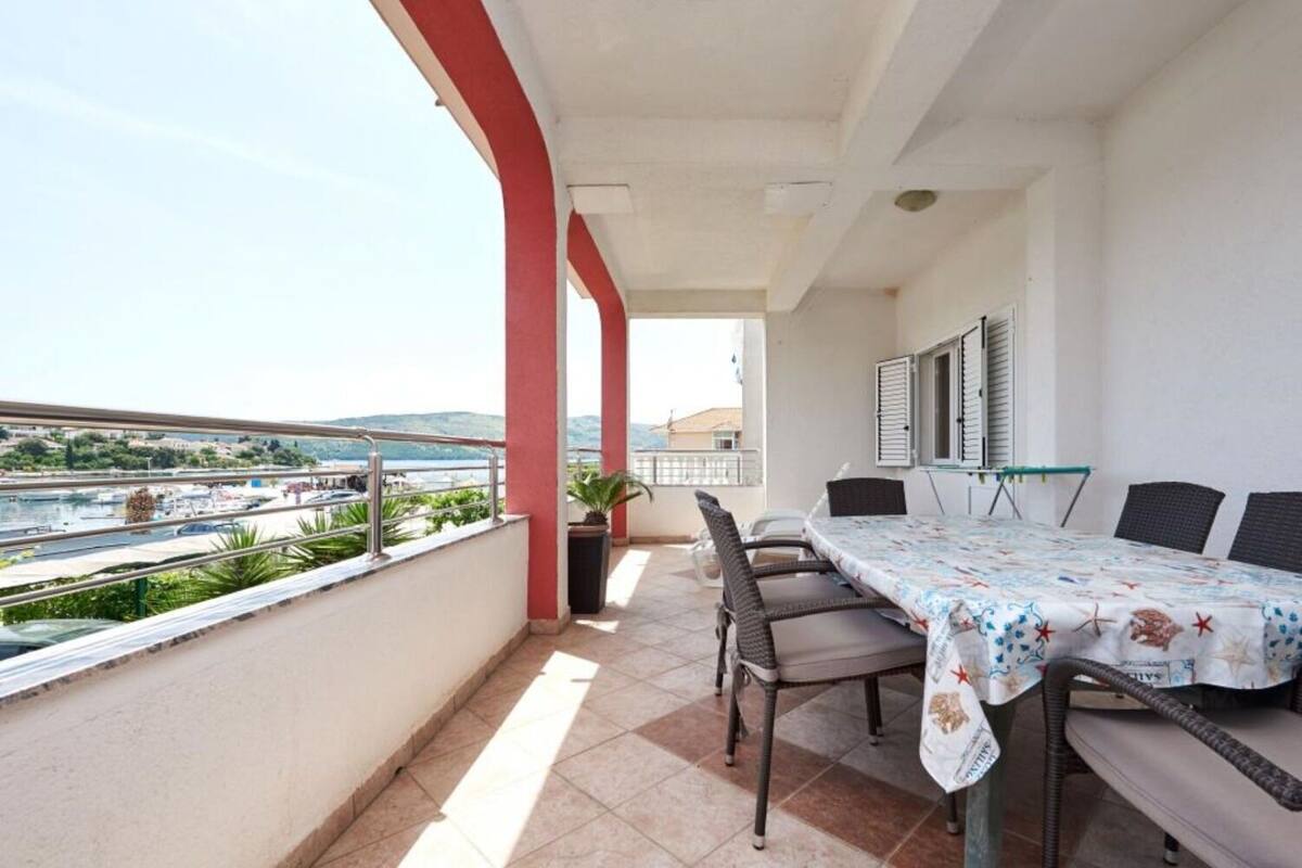A balcony with a table and chairs, a potted plant, and a view of the sea and buildings.