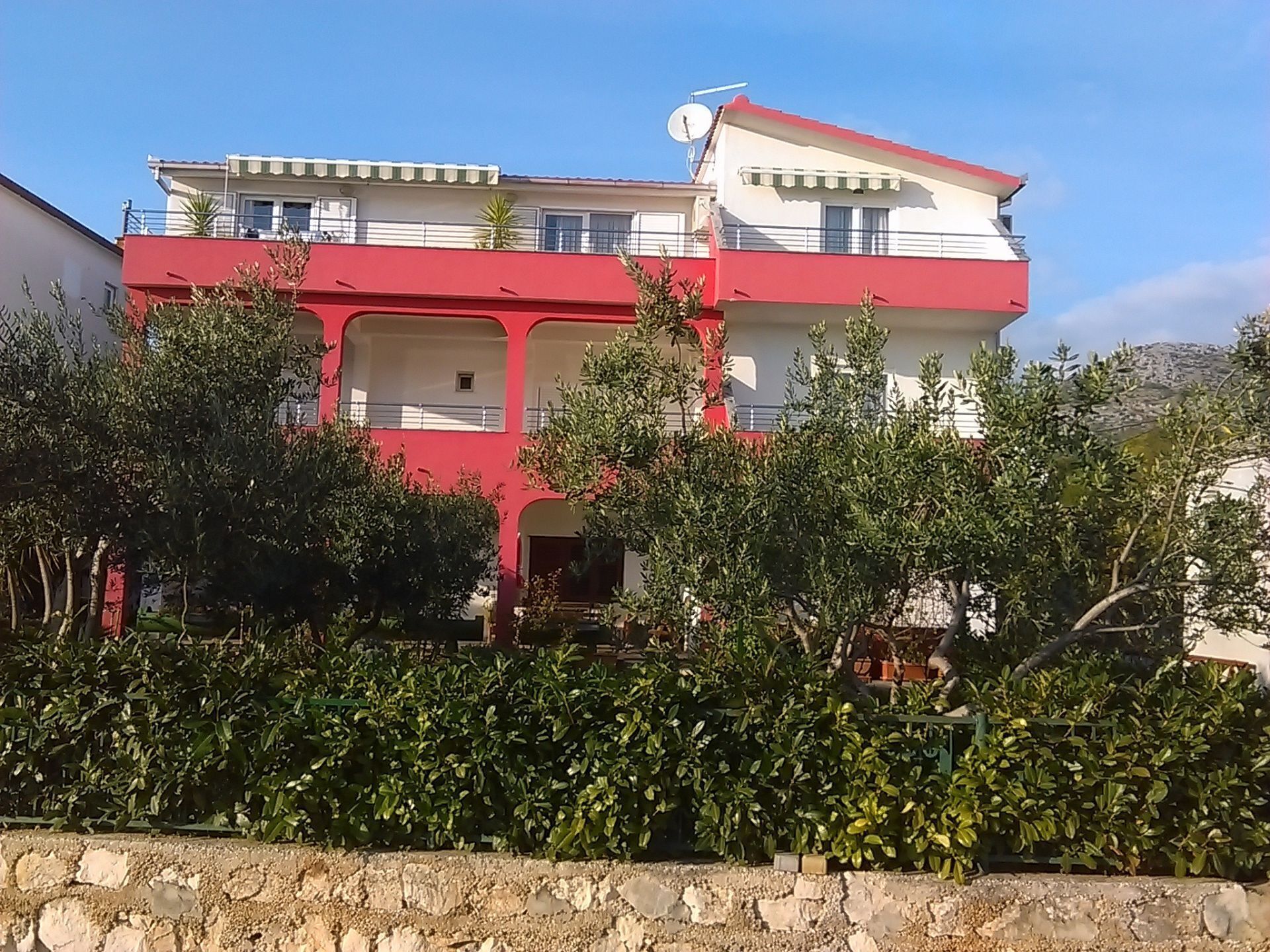 Un edificio de dos pisos con fachada roja y blanca, balcones y una antena parabólica.