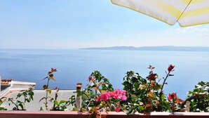 Ein Balkon mit Meerblick, ein gestreifter Sonnenschirm und Kübelpflanzen.