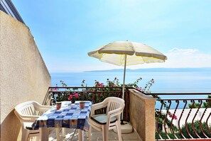 A balcony with a table and chairs, an umbrella, and a view of the sea. - Apartments Goran (Brela)
