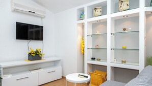 A modern living room with a flat-screen TV, white entertainment unit, glass shelves, and a sofa. - Apartments Antisa (Tucepi)