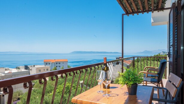 A balcony with a table, chairs, a bottle, and glasses, overlooking a coastal view. - Apartments Antisa (Tucepi)