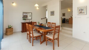 A dining area with a wooden table and chairs, a fruit bowl, and a small cabinet with a mirror. - House Dupla (Okrug)